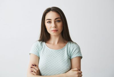 Portrait of beautiful brunette girl looking at camera with crossed arms over white background. Copy space.